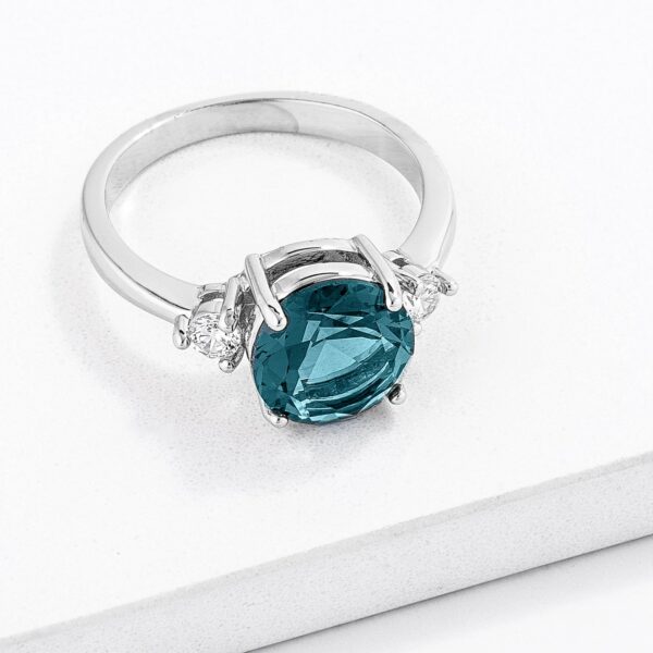 Round blue green cubic zirconia on a 3mm wide silver tone over lead free alloy (brass) three-stone ring.