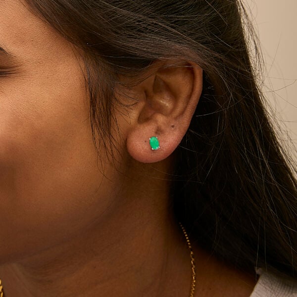 Oval green emerald stud earrings worn on a model's ear