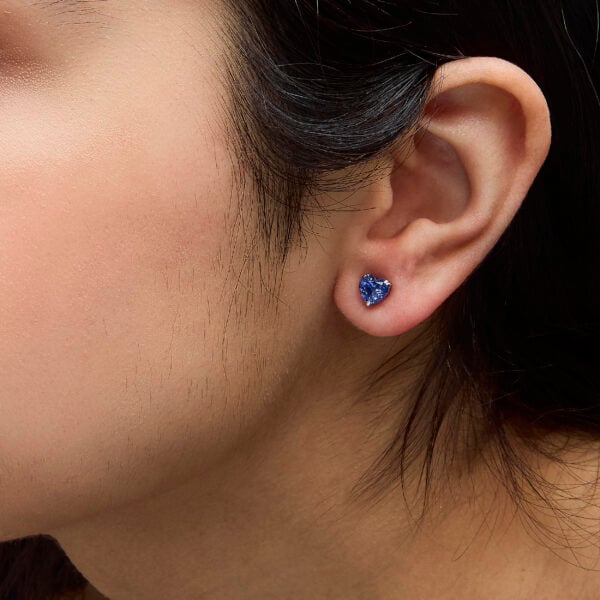 Platinum heart sapphire stud earrings worn on an ear